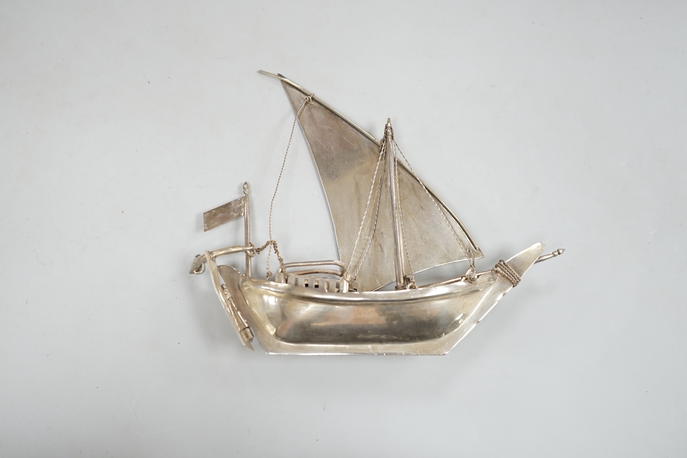 A Kuwait white metal miniature model of a sail boat, length 16cm, on wooden stand